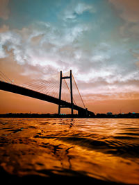 Suspension bridge over sea against sky during sunset