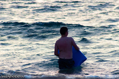 Rear view of shirtless man standing in sea