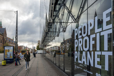 People on street amidst buildings in city against sky