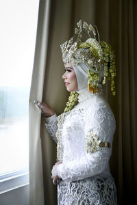 Close-up of smiling young woman standing by window