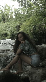 Portrait of woman sitting on rock in forest