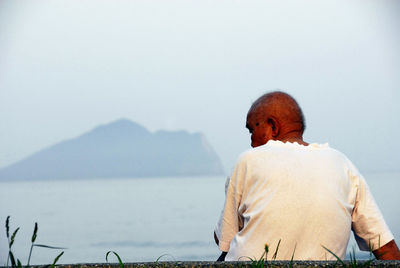 Rear view of man standing by sea against clear sky