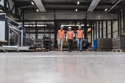 Three men wearing hard hats and safety vests walking on factory shop floor