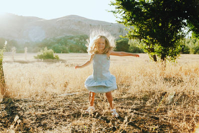 Girl with arms outstretched standing on grassy field against mountain