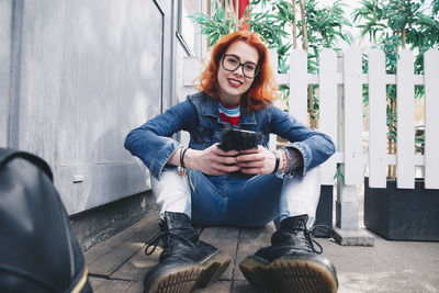 Portrait of redhead young woman using mobile phone while sitting by door