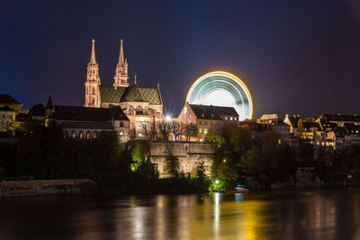 Illuminated building by river against sky at night