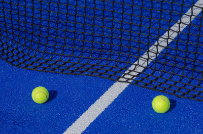 Two balls next to the service line and the net of a paddle tennis court