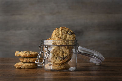 Glass cookie jar with oat and raisin homemade cookies on a wooden surface.