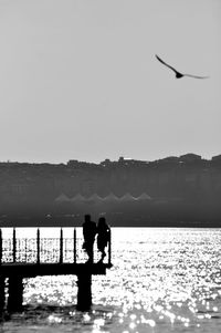 Silhouette people standing by railing on pier over lake against clear sky