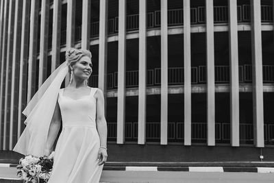 Portrait of young woman standing against building