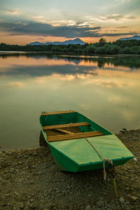 Boat moored at lakeshore against sky during sunset