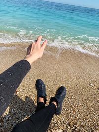 Low section of person gesturing sitting on beach