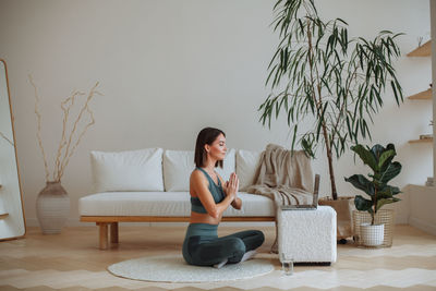 A woman is doing yoga in an online lesson on a laptop at home in the living room