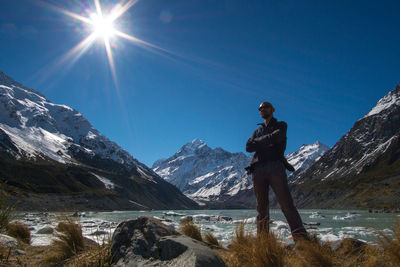 Low angle view of man standing by river against snowcapped mountain sky