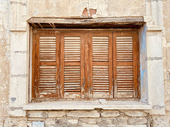 Old rustic weathered wooden window closed shutters on stone wall