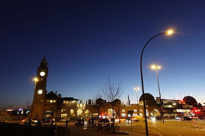 Illuminated street amidst buildings against sky at dusk