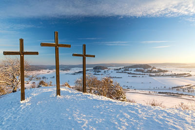 Cross on snow covered field against sky