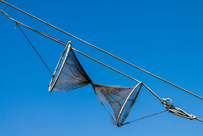 Low angle view of fishing net hanging against blue sky