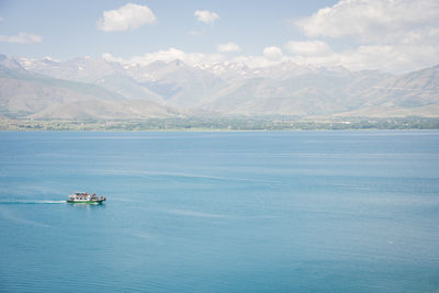 Sightseeing boat with tourists sailing on beautiful blueish lake with mountains in backdrop, turkey