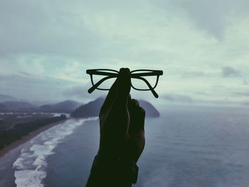 Person holding umbrella by sea against sky