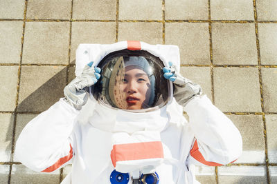 Female astronaut holding helmet while lying on footpath during sunny day