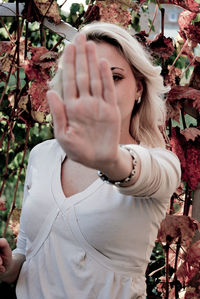 Woman gesturing stop while standing against plants