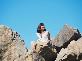 Woman sitting on rock against sky