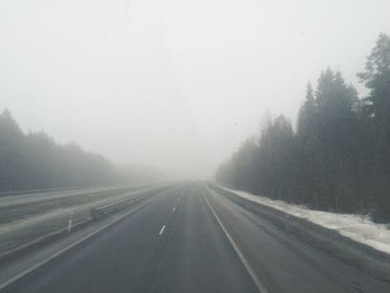 Road amidst trees against sky during winter