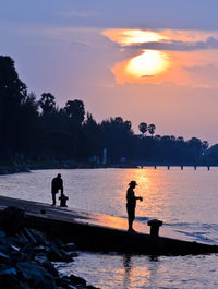 Silhouette people in swimming pool against sky during sunset