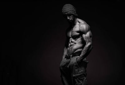 Shirtless muscular man standing against black background