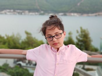 Cute thoughtful boy standing at balcony against lake