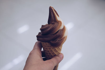 Hand holding ice cream cone against white background