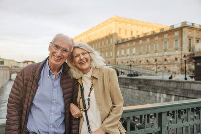 Portrait of happy senior man and woman leaning on railing in city
