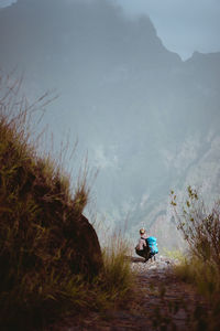 Rear view of woman crouching by cliff