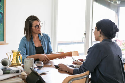 Female design professionals discussing while sitting at table in home office