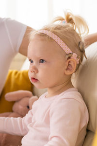 Portrait of cute baby girl looking away while sitting on bed at home