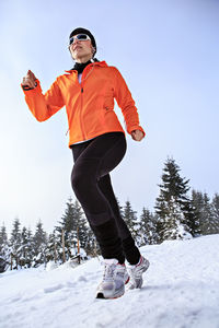 Woman running on snow covered field against sky