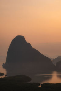 Silhouette rocks by sea against orange sky