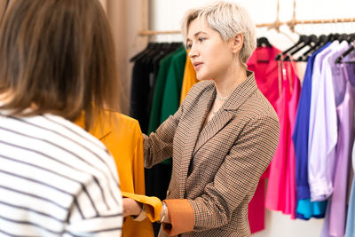 Young women choosing clothes at store, sales consultant offers wear