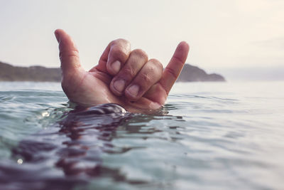 Cropped hand gesturing shaka in sea