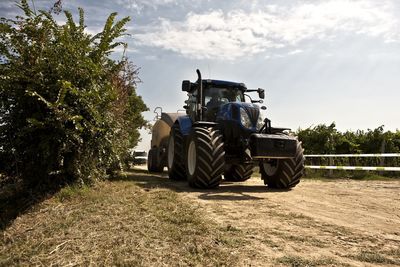 Tractor on field by road against sky