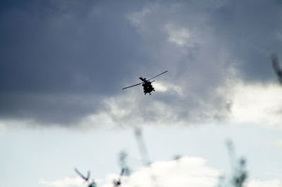 Silhouette military helicopter flying against cloudy sky