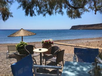 Chairs and table by sea against sky