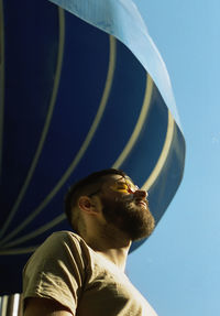 Portrait of young man looking away against blue sky