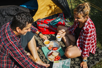 Couple having breakfast and planning their day sitting by tent at camping