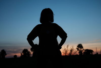 Rear view of silhouette woman standing on field against sky during sunset
