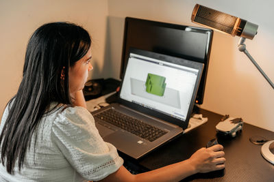 Young businesswoman sitting at desk, using laptop and 3d design software