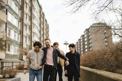 Cheerful male friends walking by building in city