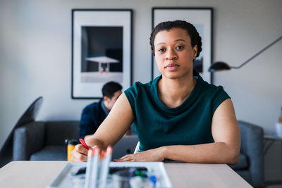 Portrait of confident businesswoman writing while sitting on table at office