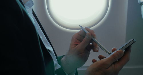 Midsection of person holding mobile phone in airplane